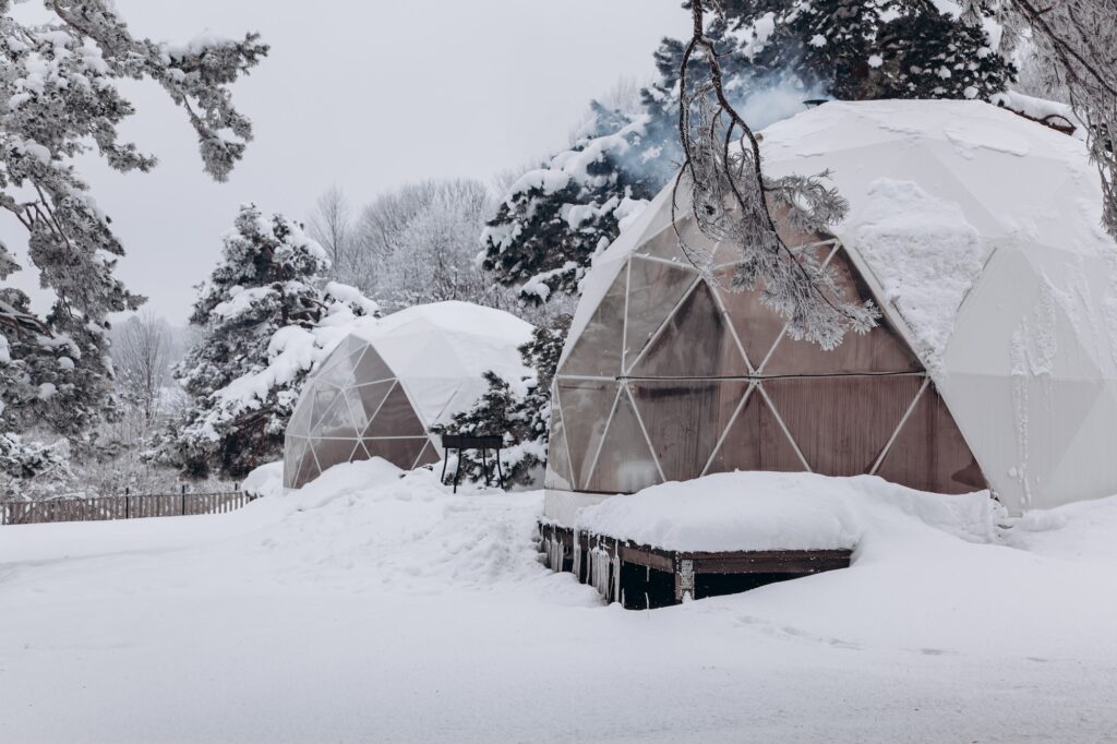 Glamping area with a dome tent and a smoking chimney from a working stove in the snowy winter